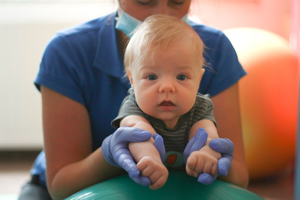 Mały pacjent pod opieką terapeuty podczas ćwiczeń na zielonej piłce rehabilitacyjnej w Ośrodku Otulinka.
