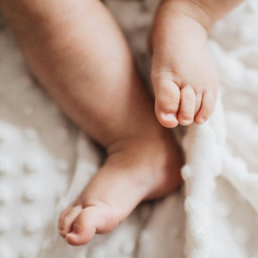 Zbliżenie na nogi niemowlaka leżącej na białej pościeli.